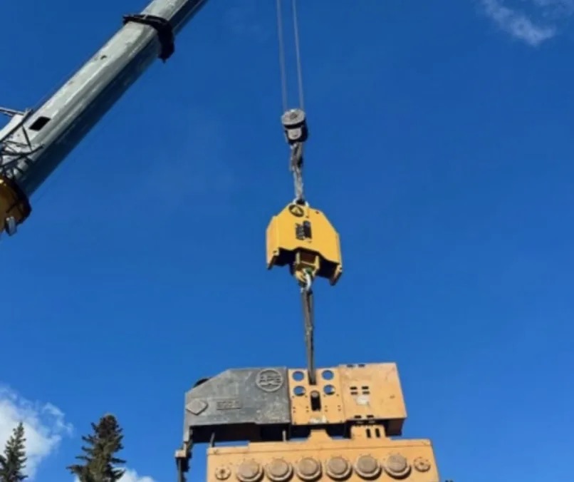 No Shock connected between crane rigging and a yellow vibratory hammer against blue sky