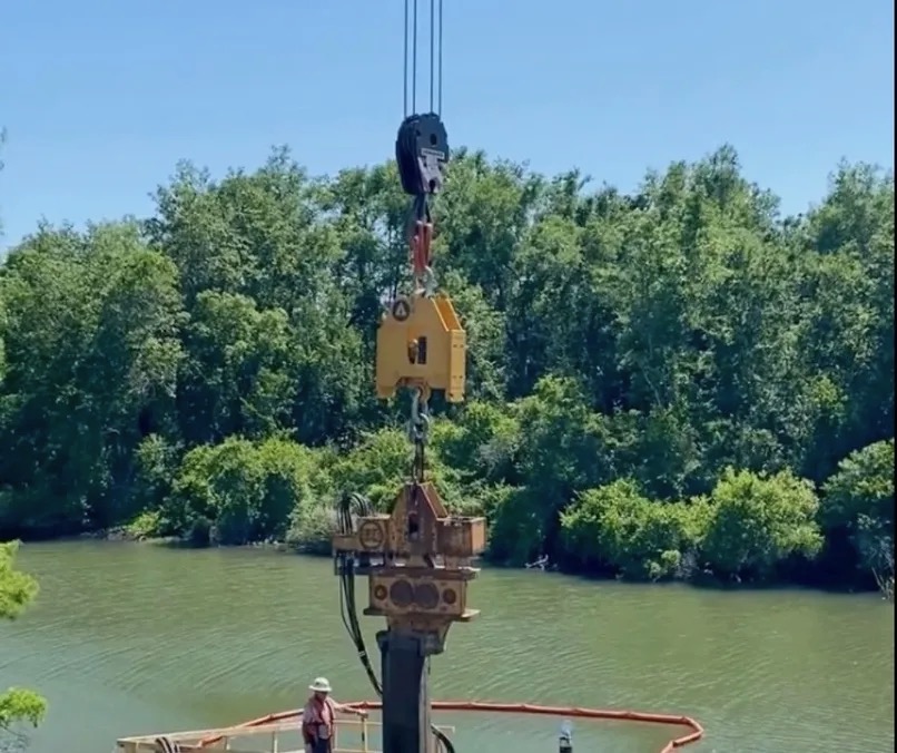 No Shock suspended above a vibratory hammer and steel pile beside the water